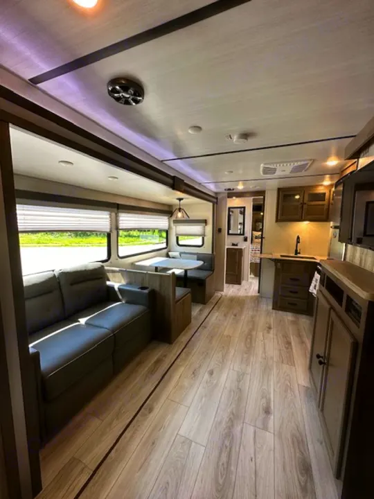 Modern RV rental interior with spacious living, dining, and kitchen areas. Light wood flooring, sofa, and booth.. Forest River Surveyor Legend 2022