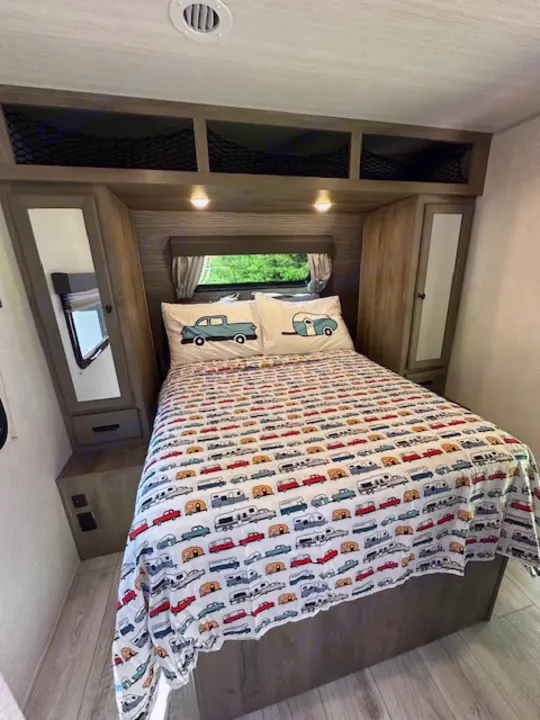 Bright RV rental bedroom featuring a bed with fun car-patterned comforter, storage shelves, and overhead cabinets.. Forest River Surveyor Legend 2022