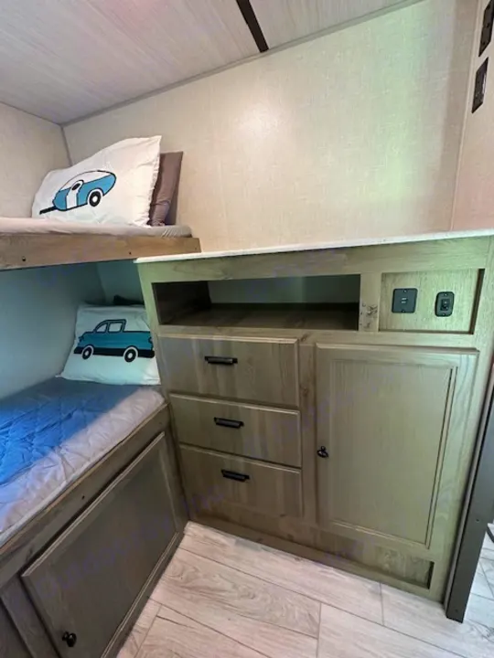An RV rental interior with compact bunk beds and integrated storage cabinets featuring a TV space and charging outlets.. Forest River Surveyor Legend 2022