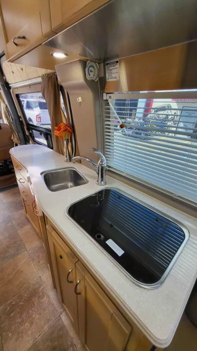 Bright RV rental kitchen showing a light countertop, stainless sink, glass stovetop, wood cabinets, & window blinds.. Mercedes AS NEW SPRINTER 4 BERTH DISCOVERY AUTO TURBO DIESEL 2013