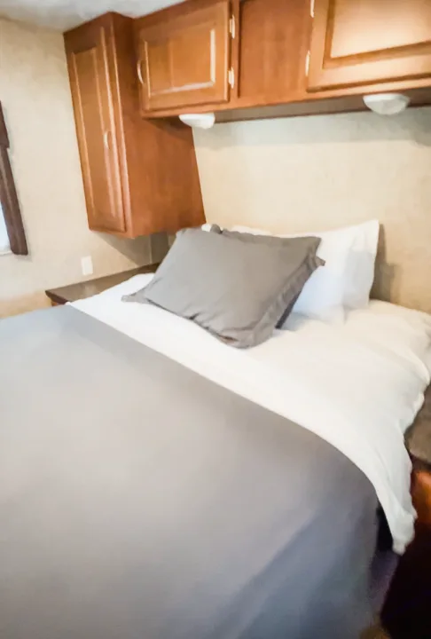 Cozy RV rental bedroom featuring a comfortable bed with grey bedding and overhead wooden cabinets, ideal for travelers.. Forest River Wildwood 2011