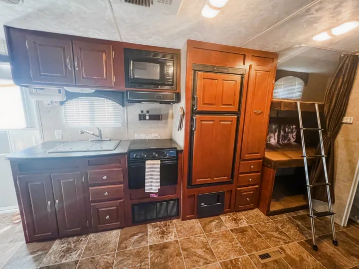 This RV rental interior showcases a full kitchen with a microwave, stove, fridge, and sink, plus cozy bunk beds.. Forest River Wildwood 2011