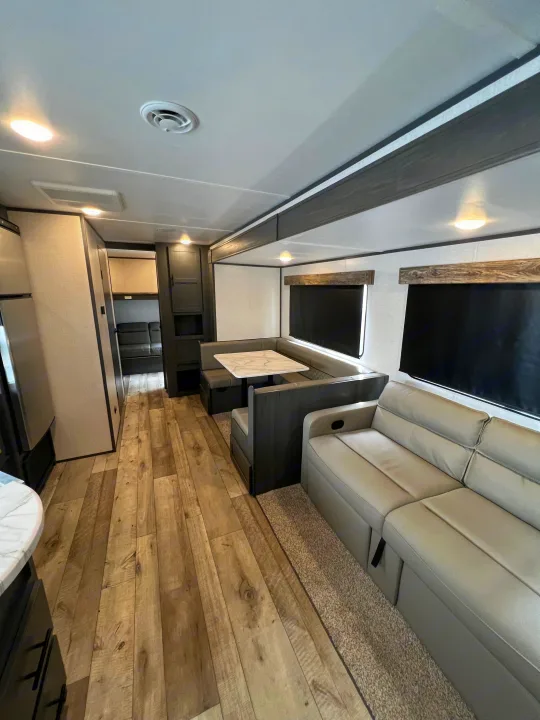 Spacious RV rental living space: modern dinette with marble table, light-colored sofa, and wood-look floors throughout.. Dutchmen Aspen Trail 2022