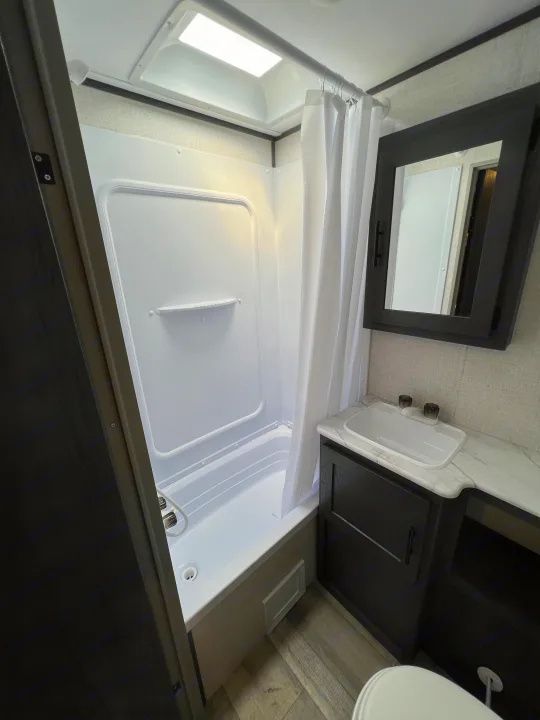 Modern RV rental bathroom interior showing a white shower/tub, sink vanity, and toilet.. Dutchmen Aspen Trail 2022