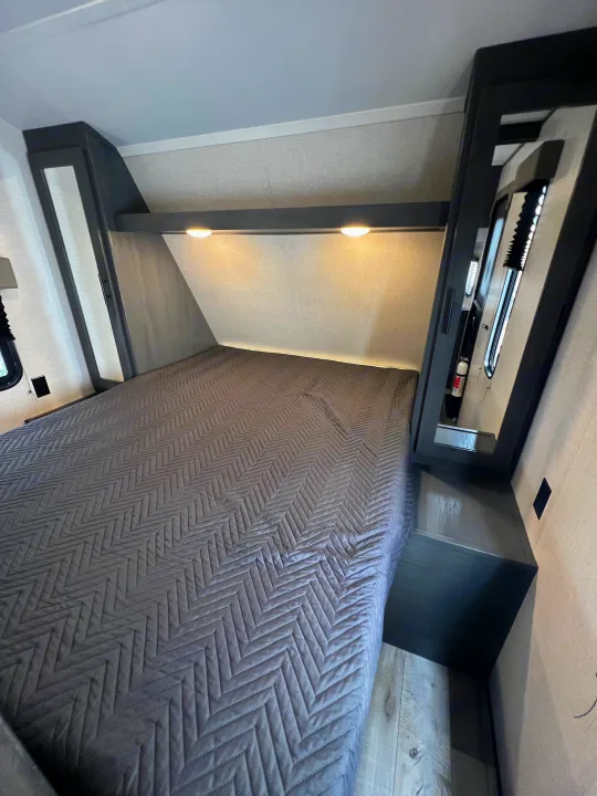 Modern RV rental bedroom showcasing a gray quilted bed, overhead lights, and built-in storage.. Dutchmen Aspen Trail 2022