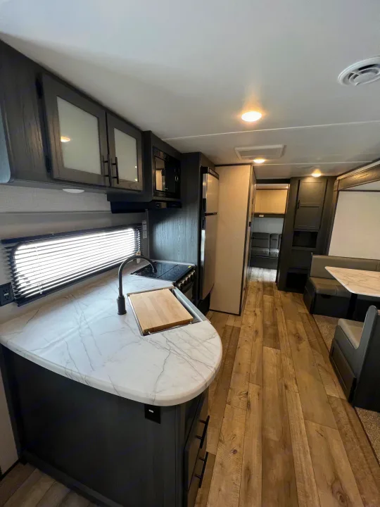 Spacious RV rental interior featuring a modern kitchen, dining booth, and living areas with light wood floors.. Dutchmen Aspen Trail 2022