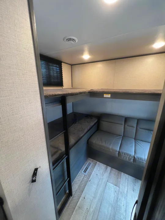 RV rental interior featuring L-shaped bunk beds with a ladder, a grey sofa, light wood-look flooring, and ceiling lights.. Dutchmen Aspen Trail 2022