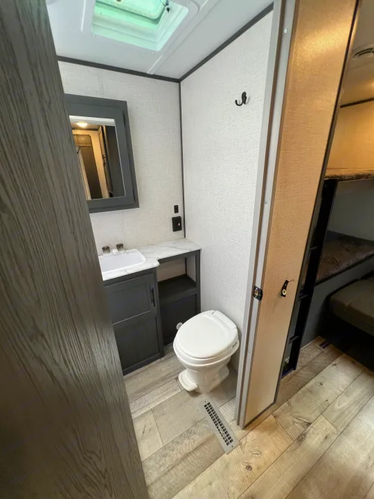 RV rental bathroom with skylight, vanity, sink, toilet, and adjacent bunk area. Modern RV interior.. Dutchmen Aspen Trail 2022