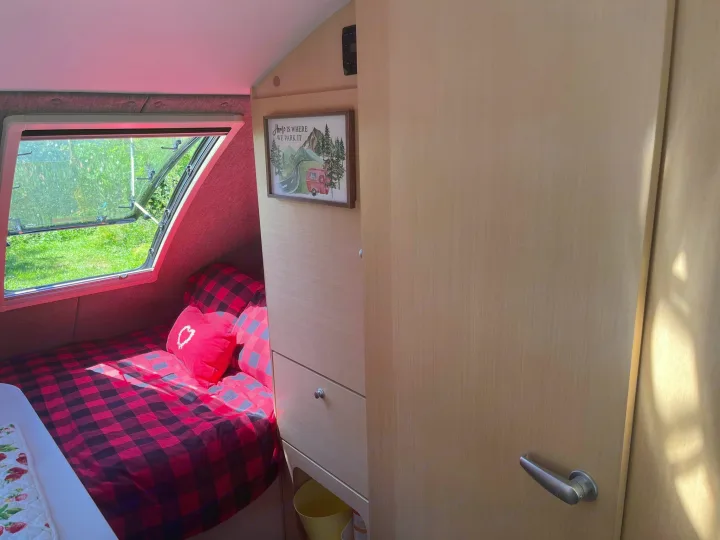 Cozy RV rental bedroom with red plaid bedding, open window to nature, and "Home is where we park it" decor.. nuCamp T@B 2020