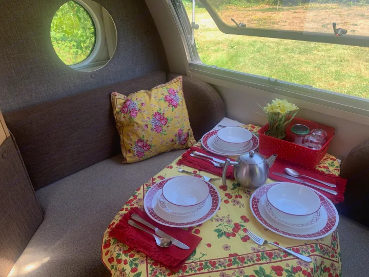 Cozy RV rental interior: A yellow table with berry print is set for two. Relax by the round window with nature views.. nuCamp T@B 2020