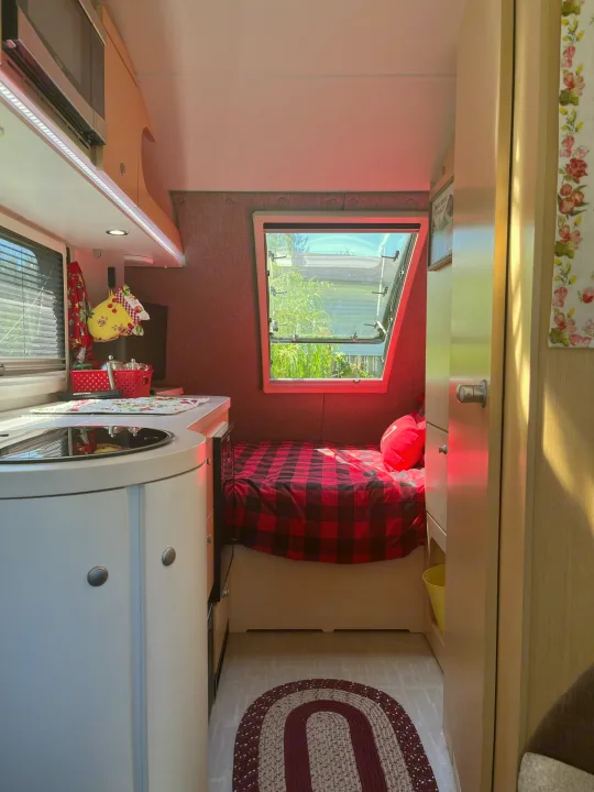 Cozy RV rental interior: compact kitchen and buffalo plaid bed bathed in sunlight. Perfect for adventure.. nuCamp T@B 2020