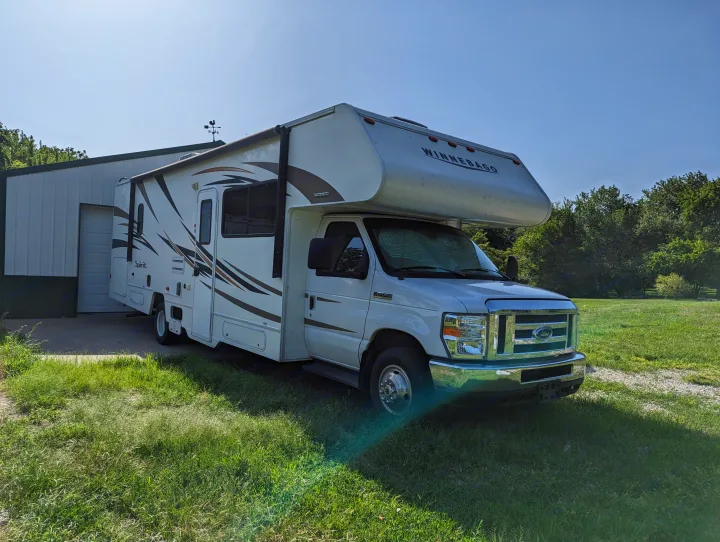 White Winnebago Spirit RV, ideal for rv rental, parked by a garage on a sunny day. Ready for your next road trip.. Winnebago Spirit 2019