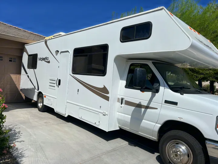 A clean, white Majestic Class C RV rental, built on a Ford E-450 chassis, is parked on a sunny driveway.. Thor Majestic 2013