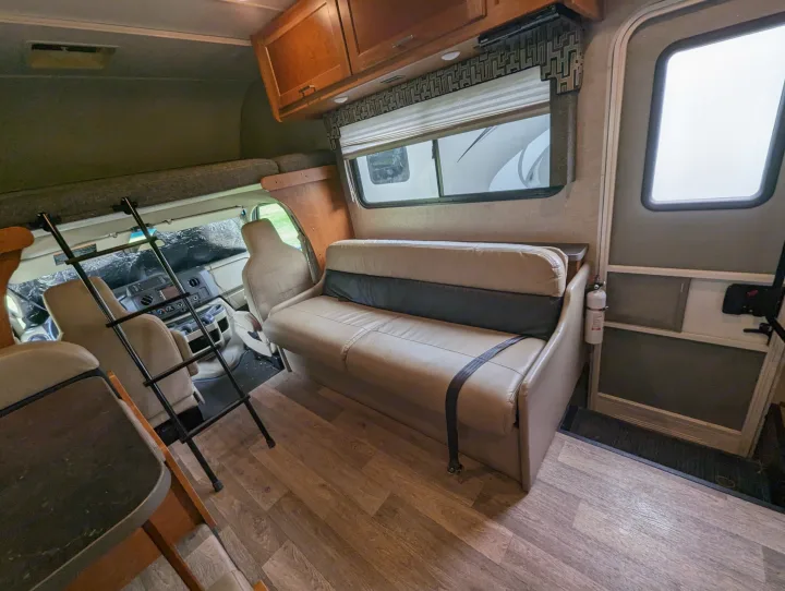 Inside an RV rental: a comfy sofa, overhead bunk with ladder, driver's cab, and fire extinguisher near the door.. Winnebago Spirit 2019
