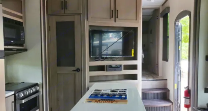 Inside a modern RV rental featuring a full kitchen, entertainment center, central island, and steps to another area.. Keystone Carbon 2020