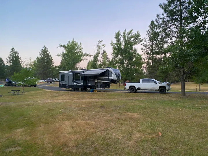 Gray fifth wheel RV rental & white truck at a grassy campground with trees, awning extended.. Keystone Carbon 2020