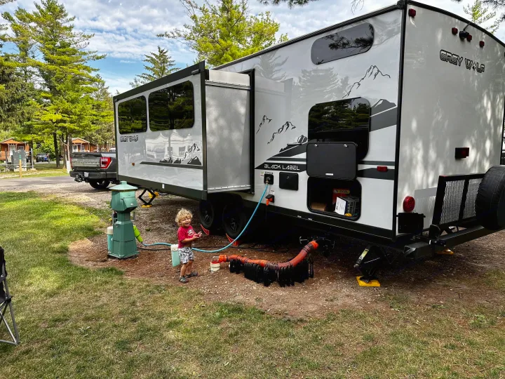 Child plays near a Grey Wolf RV rental at a scenic campground, complete with essential hookups.. Forest River Cherokee Grey Wolf Black Label 2021