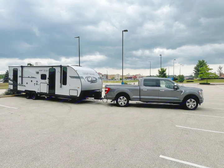 A gray pickup truck tows a "Grey Wolf" travel trailer in a parking lot, ready for an RV rental adventure.. Forest River Cherokee Grey Wolf Black Label 2021