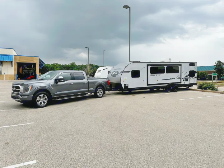 Grey Ford F-150 pickup towing a Grey Wolf RV travel trailer, parked under dark skies. Perfect for an RV rental.. Forest River Cherokee Grey Wolf Black Label 2021