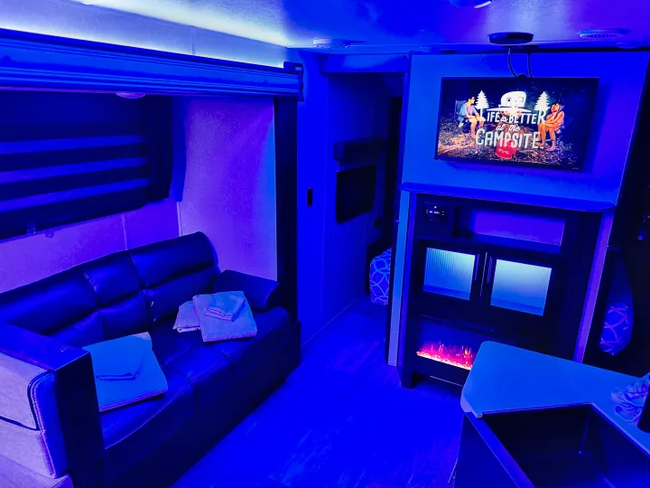 Cozy RV rental interior at night, bathed in blue ambient light. Features a comfy sofa, entertainment system with TV and fireplace, and kitchen area.. Forest River Cherokee Grey Wolf Black Label 2021