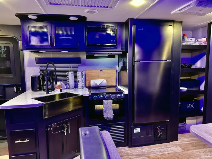 Sleek rv rental kitchen with dark cabinets, modern appliances, a sink, stove, and fridge, illuminated by blue light.. Forest River Cherokee Grey Wolf Black Label 2021