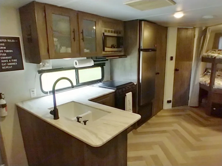 Explore this cozy RV rental's kitchen and living area, complete with a sink, stove, fridge, and bunk beds.. Forest River Wildwood X-Lite 2020