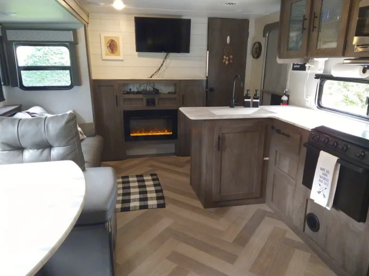 Inside a modern RV rental: a compact kitchen, comfortable seating, and a built-in electric fireplace create a cozy living space.. Forest River Wildwood X-Lite 2020