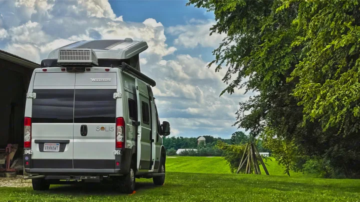 A white Winnebago Solis camper van, great for rv rental, parked in a scenic green field, under a cloudy sky, ready for trips.. Winnebago Solis 2021
