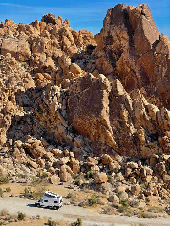 White RV rental parked in a rugged desert landscape among massive rock formations under a clear blue sky.. Winnebago Solis 2021