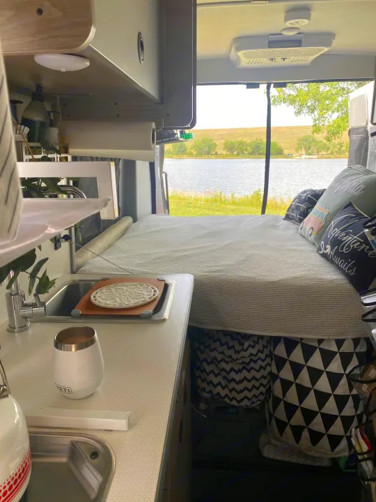Cozy RV rental interior with a comfy bed, kitchenette, and a beautiful lake view out the back doors.. Winnebago Solis 2021