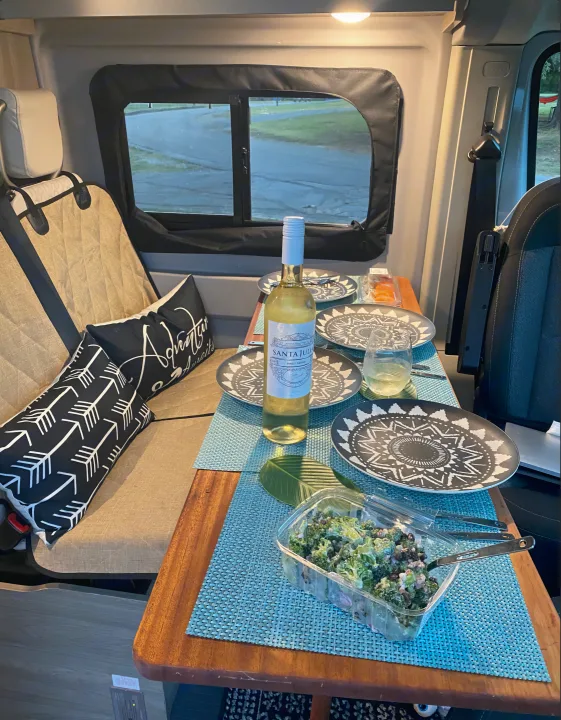 Cozy RV rental interior with wine, salad, and dinnerware set for a relaxing meal.. Winnebago Solis 2021