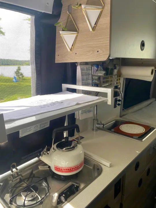 Compact RV rental kitchen with stove, sink, and lake view, perfect for camper adventures.. Winnebago Solis 2021