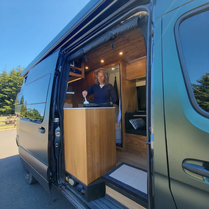 Woman enjoys cooking in her modern camper van, perfect for a comfortable RV rental experience & outdoor adventures.. Mercedes-Benz Sprinter 2020