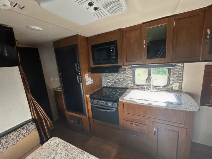 Spacious **RV rental** kitchen with a two-door fridge, stove, microwave, and sink. Wooden cabinets and a window create a cozy interior.. Forest River Wildwood X-Lite 2017