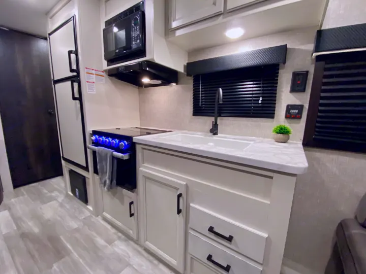 Step inside this modern RV rental kitchen featuring white cabinets, black appliances, a sleek sink, and illuminated stove knobs.. Jayco Jay Flight 2023