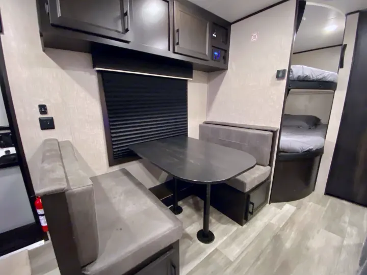RV rental interior: a dinette with table, overhead cabinets, window, and nearby bunk beds visible. Includes control panel & fire extinguisher.. Jayco Jay Flight 2023