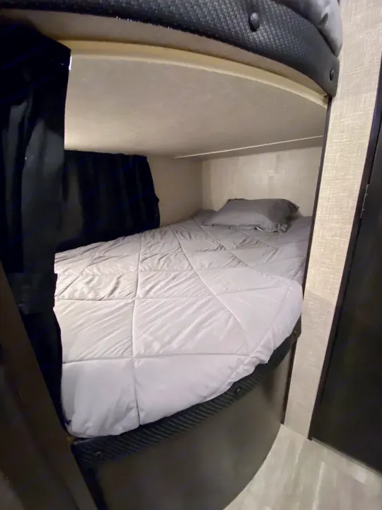 Cozy RV rental bunk bed with grey comforter and privacy curtain.. Jayco Jay Flight 2023