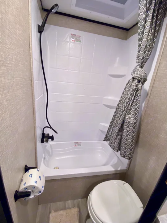 Compact RV rental bathroom showcasing a white shower/tub, black fixtures, patterned curtain, and toilet.. Jayco Jay Flight 2023