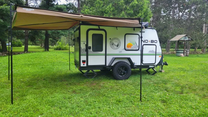 Enjoying the outdoors with an RV rental: a compact white No Boundaries camper with its side awning extended on green grass.. Forest River NoBo 10.6 2022