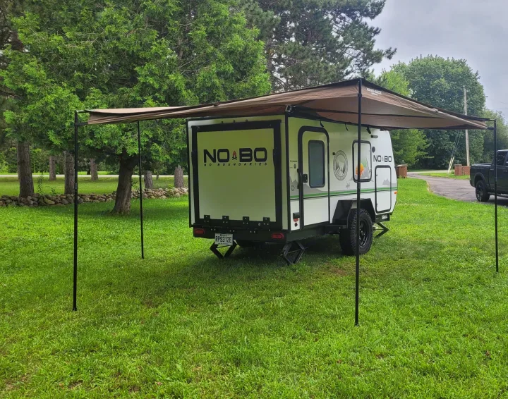 This compact No Boundaries camper, an ideal rv rental, is parked on a lush lawn with its large awning extended for shade.. Forest River NoBo 10.6 2022