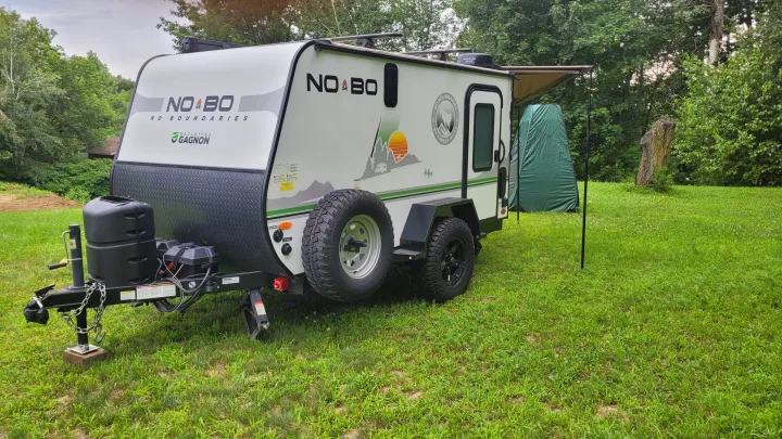 Compact No Boundaries RV rental with awning extended on a green campsite, surrounded by trees. Ideal for outdoor adventures.. Forest River NoBo 10.6 2022