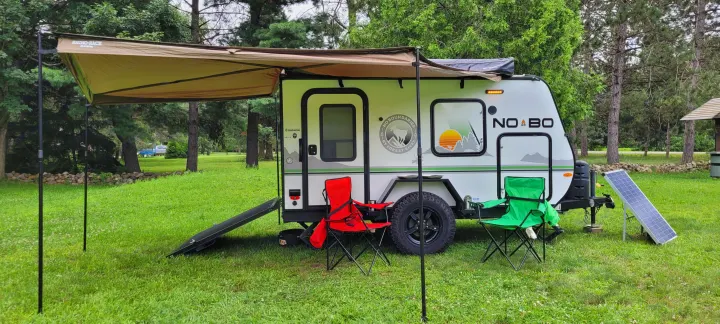 Compact NOBO travel trailer setup with awning, solar panel, and chairs at a lush campsite, perfect for an RV rental adventure.. Forest River NoBo 10.6 2022