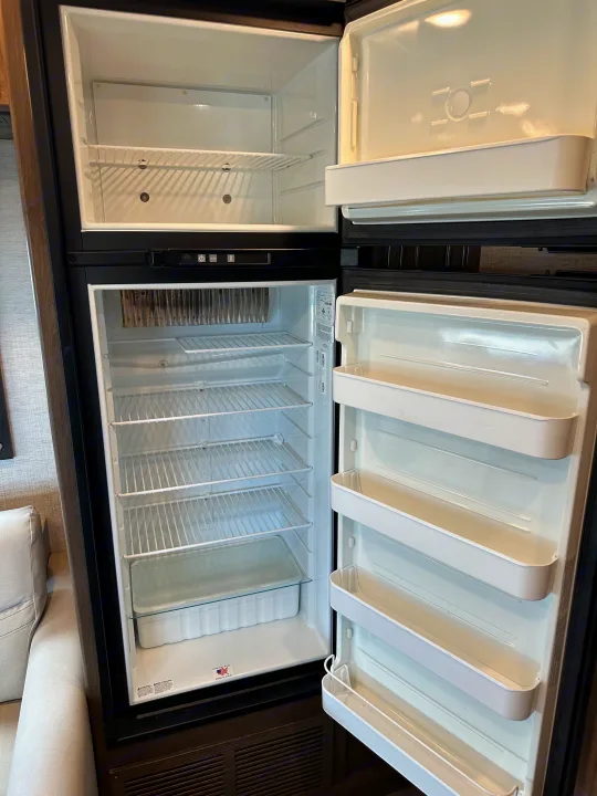 Empty two-door refrigerator with top freezer in an RV rental, ready for your trip. Doors open, shelves visible.. Jayco Redhawk 2021