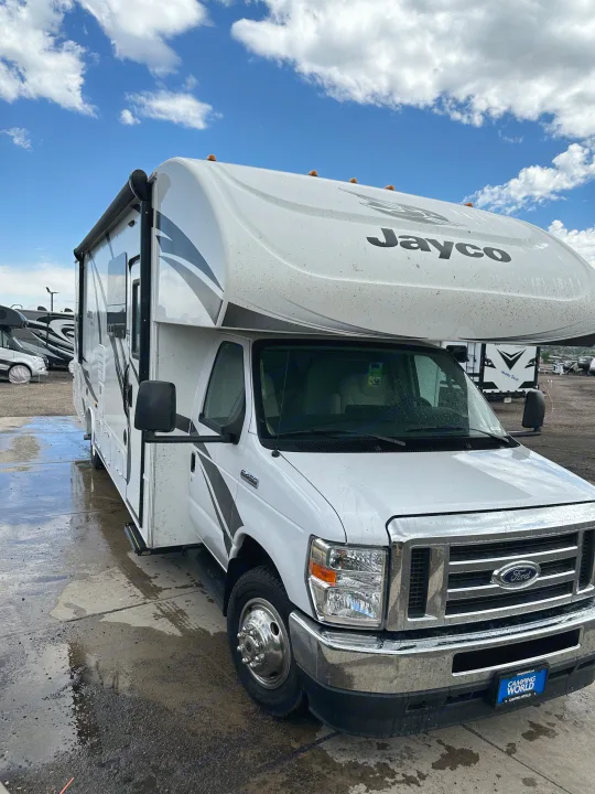 A white Jayco Class C rv rental, a Ford E450 model, sits on a wet lot under a cloudy sky, ready for adventure.. Jayco Redhawk 2021