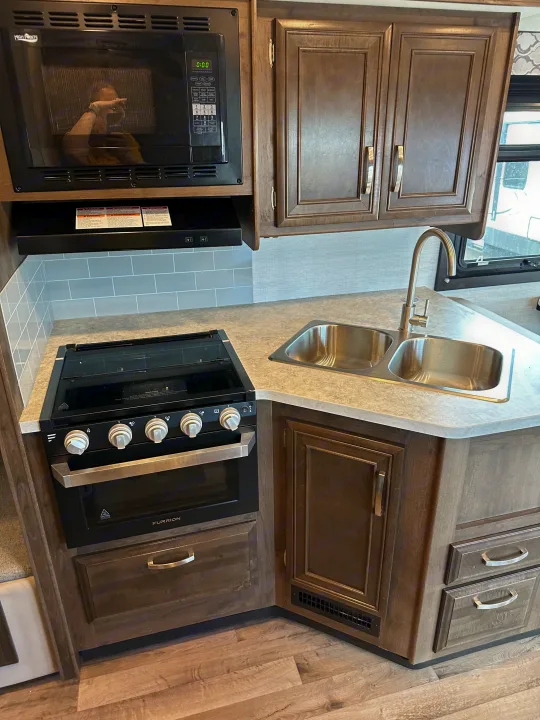 RV rental kitchen showing microwave, stove, double sink, and wood-grain cabinets, ideal for travel cooking.. Jayco Redhawk 2021