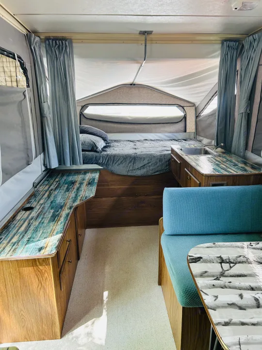 Cozy pop-up RV rental interior with bed, custom counters (sink, dining), and blue accents. Ready for your trip!. Cobra Flagstaff 1995
