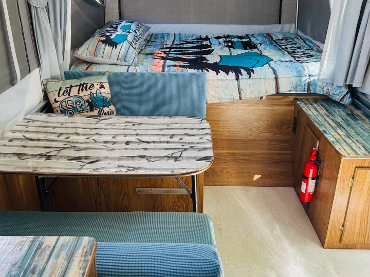 "Let the adventure begin" in this cozy RV rental, featuring a bed, dinette with patterned table, and blue seating.. Cobra Flagstaff 1995