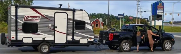 Coleman RV rental towed by a pickup truck. A family prepares for their road trip with bikes in the truck bed.. Dutchmen Coleman Lantern LT 2017