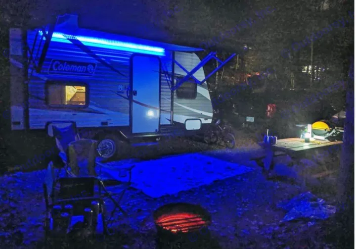 Enjoying a tranquil RV rental night. A travel trailer glows with blue lights, casting light on the campfire and campsite.. Dutchmen Coleman Lantern LT 2017
