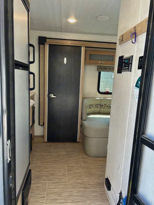Interior view of an RV rental, showing the living space with a refrigerator on the left, a dark door, and a dinette area.. R-Pod Hood River Edition 2020